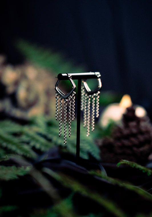 Silver hoop earrings with dangling chains on a dark background