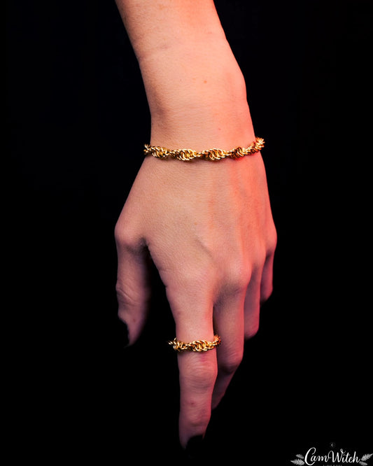Hand wearing a gold bracelet and ring against a black background